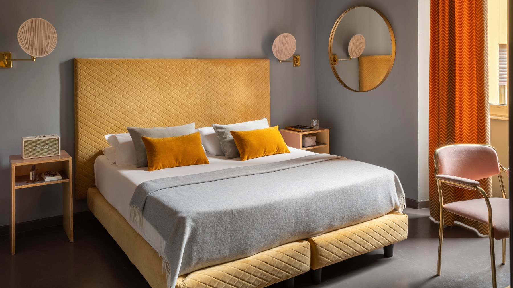 Double bed with yellow upholstered headboard and ochre pillows in hotel room - Hotel Milani, BZAR hotels in Rome